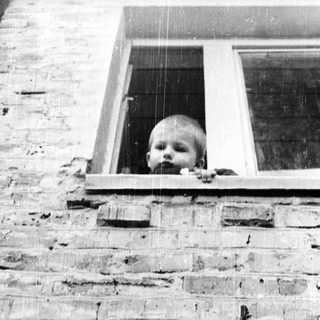 Baby peering out of a window, framed by brickwork.