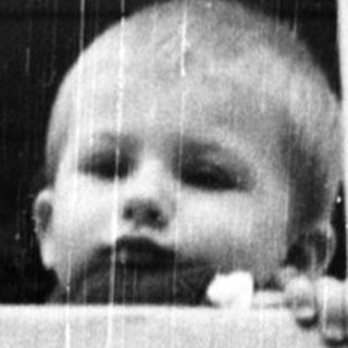 Baby peering out of a window, framed by brickwork.