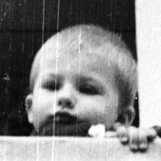 Baby peering out of a window, framed by brickwork.