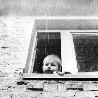 Baby peering out of a window, framed by brickwork.