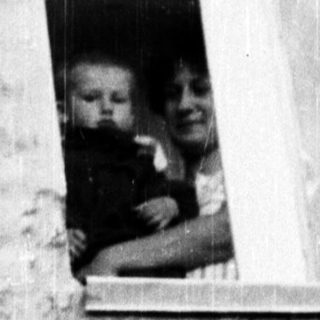 Here's a brief summary of the image: Woman holding a baby, visible in a window.