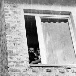 Here's a brief summary of the image: Woman holding a baby, visible in a window.