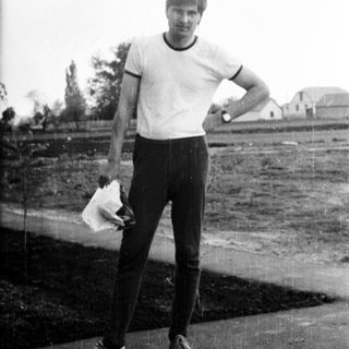 Here's a brief summary of the image: Man in sportswear stands outdoors, holding a handkerchief.