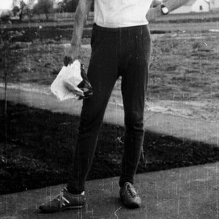 Here's a brief summary of the image: Man in sportswear stands outdoors, holding a handkerchief.