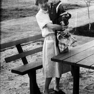 Woman holding a young child near a picnic table.