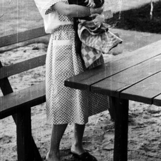 Woman holding a young child near a picnic table.