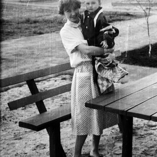 Woman holding a young child near a picnic table.