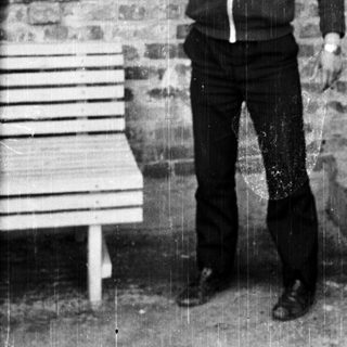 Man in tracksuit lifting dumbbell near brick wall.
