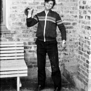 Man in tracksuit lifting dumbbell near brick wall.