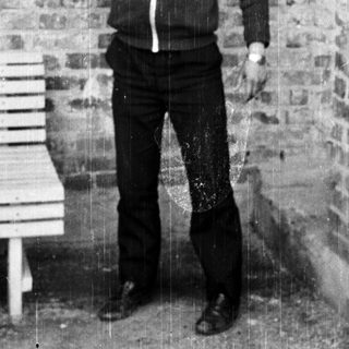Man in tracksuit lifting dumbbell near brick wall.