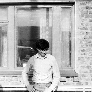 Man in glasses stands outside a brick building window.