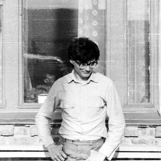 Man in glasses stands outside a brick building window.