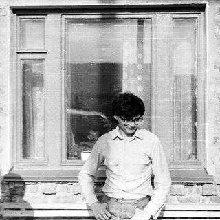 Man in glasses stands outside a brick building window.