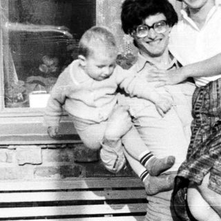 Woman holds baby outside a brick building.