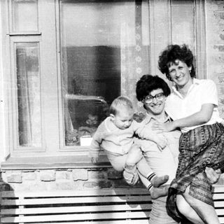 Woman holds baby outside a brick building.