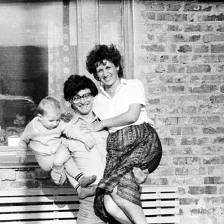 Woman holds baby outside a brick building.