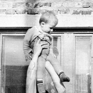 Man holds child up in front of a brick building.