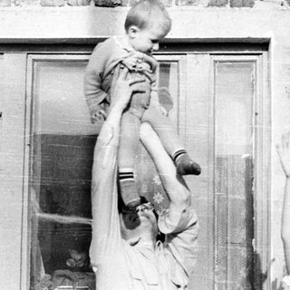 Man holds child up in front of a brick building.