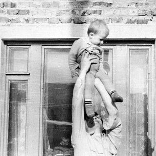 Man holds child up in front of a brick building.