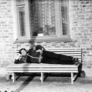 Man reclining on a bench outside a brick building.