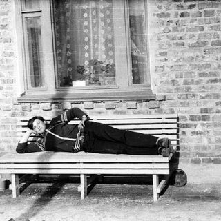 Man reclining on a bench outside a brick building.