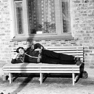 Man reclining on a bench outside a brick building.