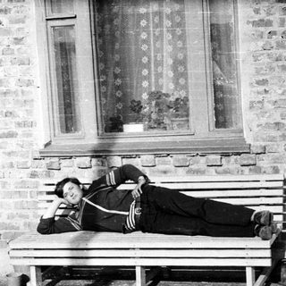 Man reclining on a bench outside a brick building.