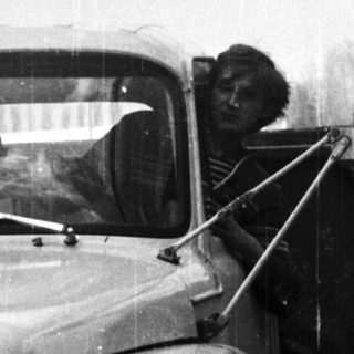 Man driving a vintage truck on a rural road.