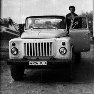 Man sitting in vintage truck, door open, black and white.