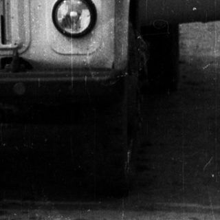 Man sitting in vintage truck, door open, black and white.