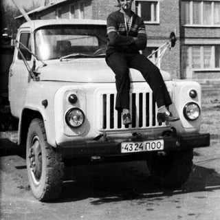 Man sits on a vintage truck in front of a house.
