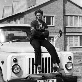 Man sits on a vintage truck in front of a house.