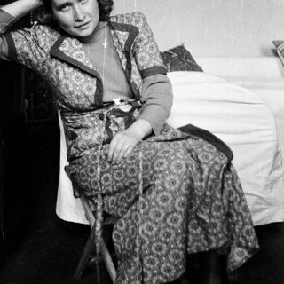 Woman seated in patterned dress, posing in a room.