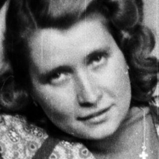 Woman seated in patterned dress, posing in a room.