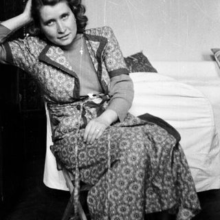 Woman seated in patterned dress, posing in a room.