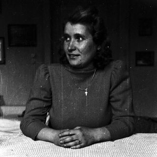 Here's a brief summary of the image: Woman wearing a sweater sits on a bed.