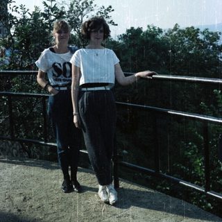 Two young women stand on a ledge overlooking greenery.