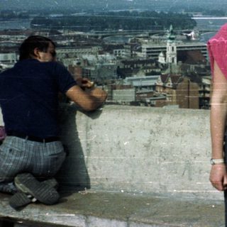 People overlooking Budapest from a rooftop, likely tourists.