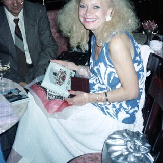 Woman with large hair holds gift, man nearby.