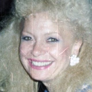 Woman with large hair holds gift, man nearby.
