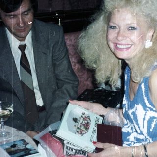 Woman with large hair holds gift, man nearby.