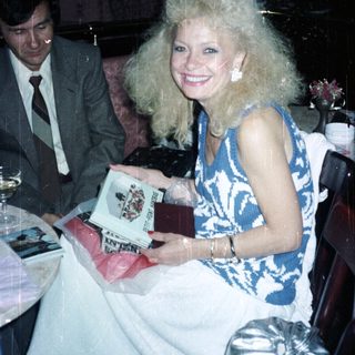 Woman with large hair holds gift, man nearby.