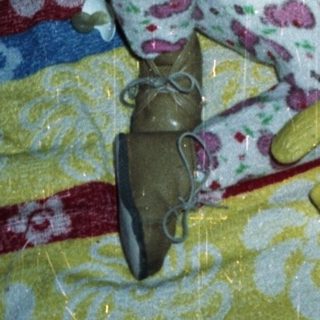 Baby sits in crib with toy and patterned blanket.