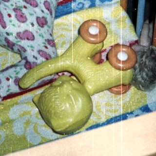 Baby sits in crib with toy and patterned blanket.