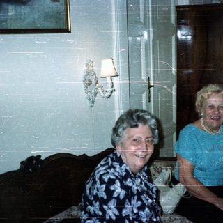 Two smiling women seated in a vintage-style living room.