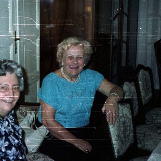 Two smiling women seated in a vintage-style living room.