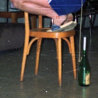 Here's a brief summary of the image: Man seated, others balance bottles on chairs in a room.