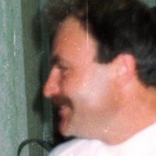 Man sits, woman stands behind him in a room.