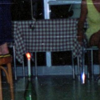 People play a game balancing bottles on chairs indoors.