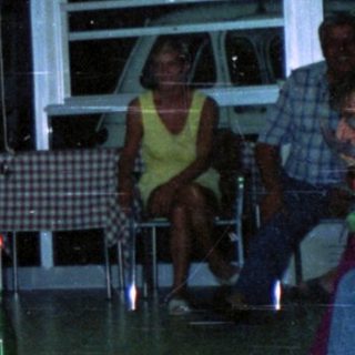 People play a game balancing bottles on chairs indoors.